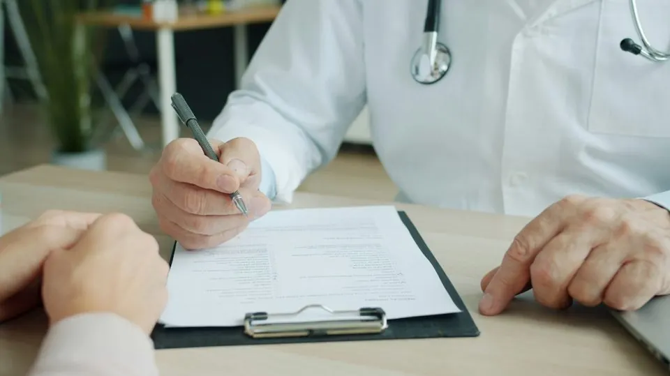 Médecin remplissant un document sur un bloc-notes pendant une consultation, face à un patient