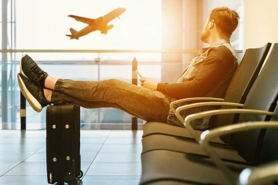 Voyageur assis dans un terminal d'aéroport, les pieds sur sa valise, regardant un avion décoller